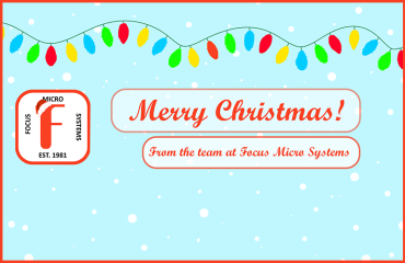 An graphic with a light blue background, with white of snowflakes. There is a string of fairy lights across the top of the image. The image features a logo of a Red 'F' with a Santa hat on it, surrounded by the words 'Focus Micro Systems Est. 1981', and wishes the reader a Merry Christmas.