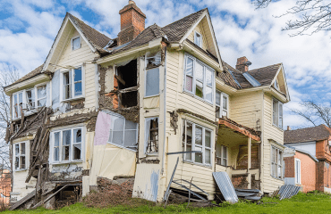 A pale yellow townhouse in disrepair due to lack of property maintenance.