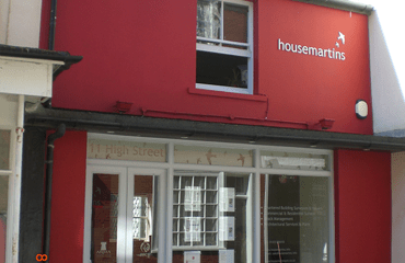 Housemartins office. A small, dark pink terraced high street building, with wide white windows, and the Housemartins logo on the top right.