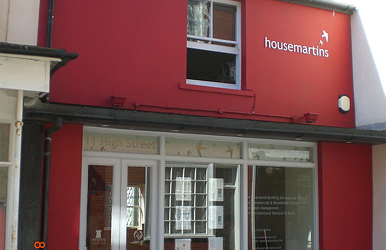 Housemartins office. A small, dark pink terraced high street building, with wide white windows, and the Housemartins logo on the top right.