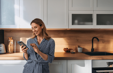 A tenant, who is looking at their phone whilst stood in a modern kitchen. They are satisfied as a result of effective tenant communication.