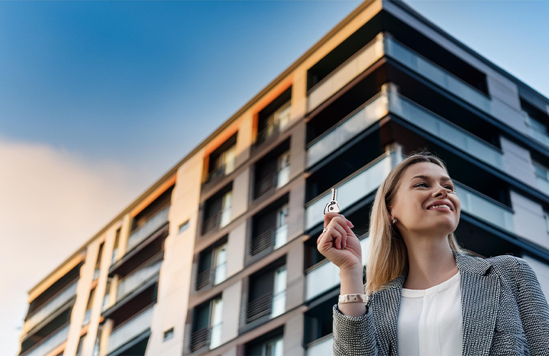 A new buy-to-let landlord, stood outside a modern block of flats, holding a key and landlords.
